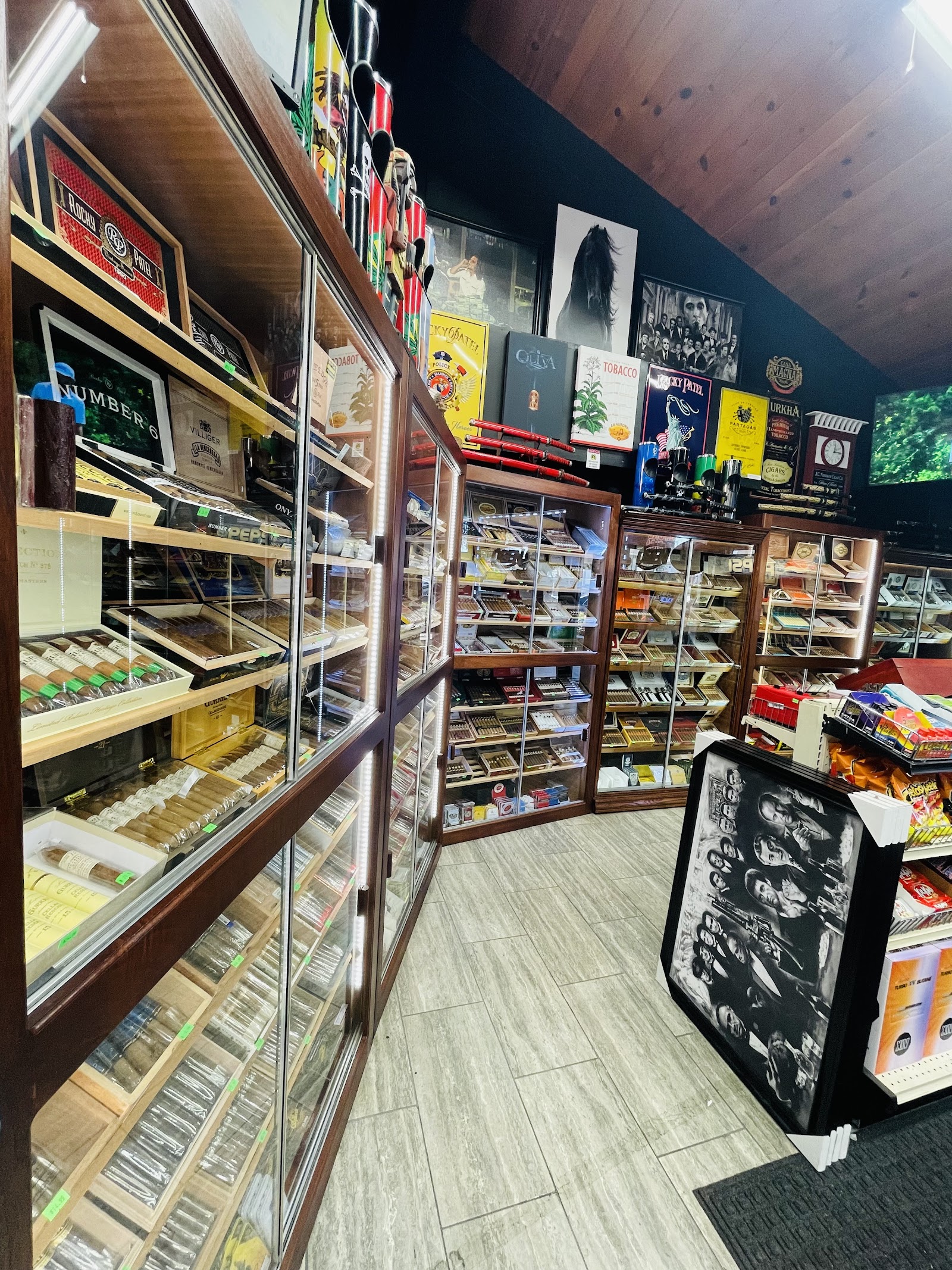 Looking down the humidor aisle: glass cabinets stacked with cigar boxes under a warm wood-plank ceiling and dark teal walls.